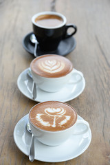 Three cofffee cup with latte art rose flower shape in the first cup another cup is hearth and leaf pattern,the last in black cup is black coffee