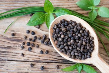 Black peppercorns in wooden spoon on rustic table with fresh basil and green onion