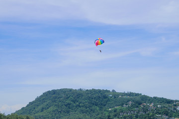 Parachute floats in the sky above the green mountains.