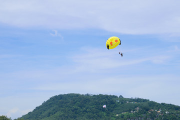 Parachute floats in the sky above the green mountains.