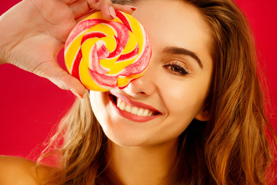Young pretty smiley woman holding lollipop in hands over red background