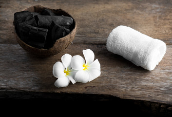 charcoal in coconut shell for spa on the wood background with white towel and flower on banana leaf for advertisement