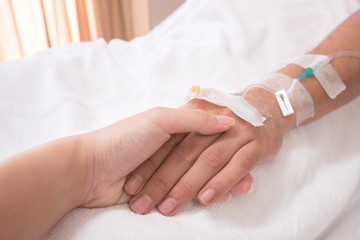 Female holding male hand, a patient in hospital
