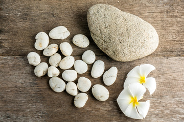 Fototapeta na wymiar White flower and leafs with big and tiny stone and towel on wood table for health spa advertisement and presentation