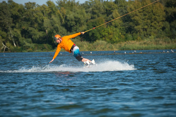 Wakeboarder, in orange shirt, turns by hand touching water spray