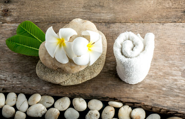 Obraz na płótnie Canvas White flower and leafs with big and tiny stone and towel on wood table for health spa advertisement and presentation