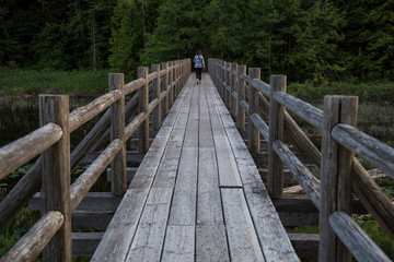 Wooden bridge across swampy water with woman walking across it. Taken in Brohm Lake, between Squamish and Whistler, North of Vancouver, BC, Canada.