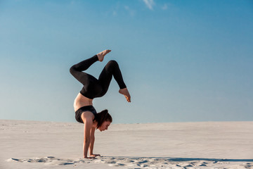 Fototapeta na wymiar Young woman practicing handstand on beach with white sand and bright blue sky