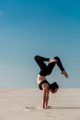 Young woman practicing handstand on beach with white sand and bright blue sky