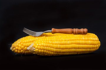 yellow fresh corn with fork on black background