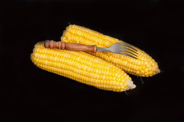 yellow fresh corn with fork on black background