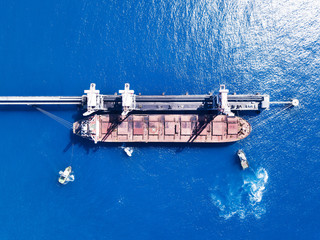 Large bulk carrier ship pulled by tow tugboats in the port near the power station dock - top down aerial shot