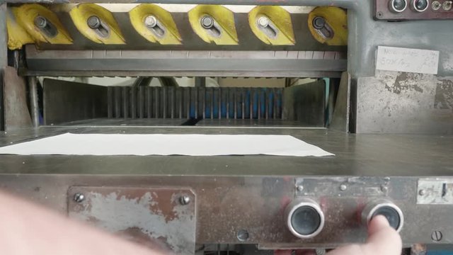Caucasian man controls old guillotine papper cutter with the help of black buttons