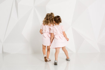 Fototapeta na wymiar Two little funny and laughing girl in gently pink dresses playing in white studio
