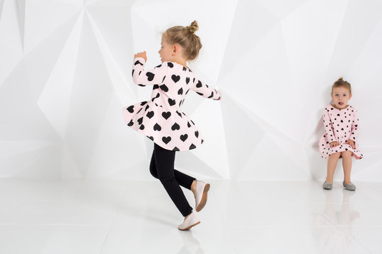 Two little funny and laughing girl in gently pink dresses playing in white studio