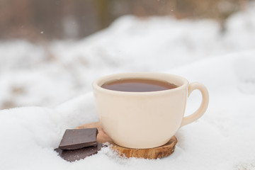 Nice warm cup of tea or coffee outdoors on the snow on a background of a winter landscape. Cozy winter still life.