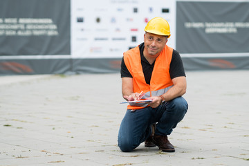 Male civil engineer wearing protective vest and hardhat working crouched on construction site