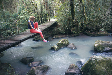 young sad woman sitting on wooden bridge over the water