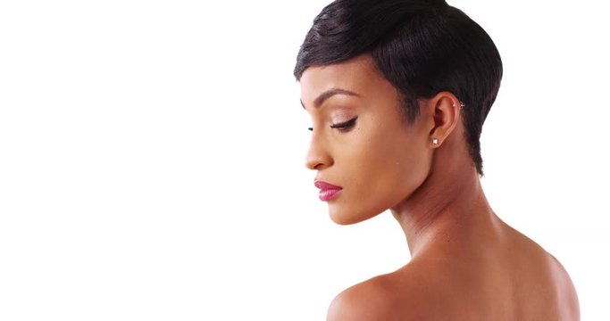 Close up of gorgeous black female with bare shoulders looking down on white background. Portrait of lovely African American woman in her 20s modeling in studio with copyspace 