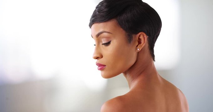 Close up of gorgeous black female with bare shoulders looking down. Portrait of lovely African American woman in her 20s modeling 