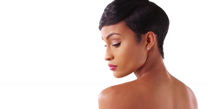 Close up of gorgeous black female with bare shoulders posing on white background with copyspace. Portrait of lovely African American woman in her 20s looking over her shoulder in studio 