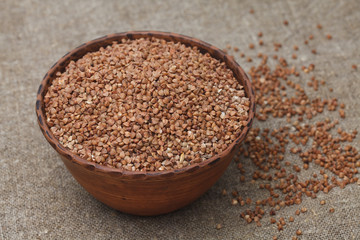 Healthy buckwheat groats in bowl on the burlap background closeup