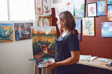 Naklejka premium Portrait of young beautiful middle age white Caucasian woman artist drawing painting in art studio with acrylic paints on canvas. Lifestyle activity hobby concept