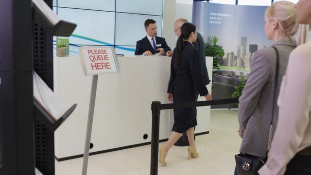  Friendly bank worker assisting queue of customers with enquiries