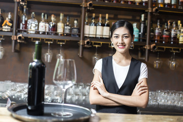 Young Asian Woman Waiter Restaurant Catering Service Happy Emotion. Woman Waiter Present Red-Wine for Customer at Bar. Woman with Wine in Bar Concept.