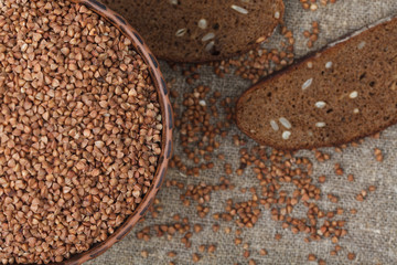 Buckwheat groats in bowl and bit of bread on the burlap background closeup