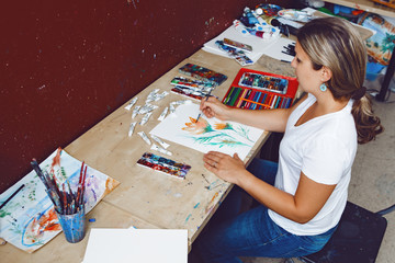 Portrait of Caucasian female artist painting flowers with watercolor paints and colored pencils. Woman painter at work in art studio. Lifestyle and hobby concept