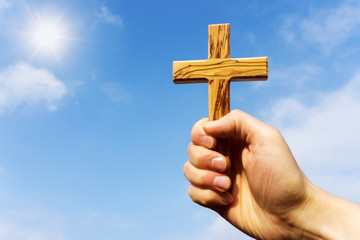 preacher holding wooden cross against blue sky