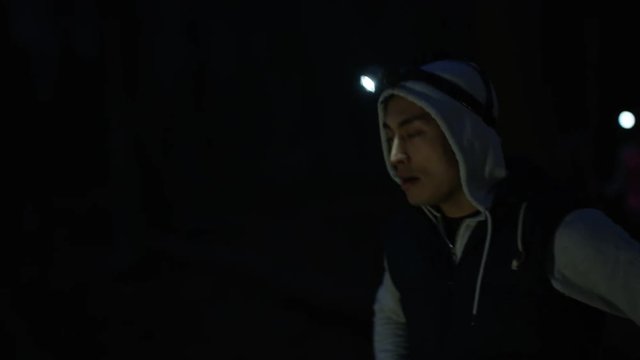 Group running in the woods at night wearing lamps on headgear, man stops to check his smartwatch.