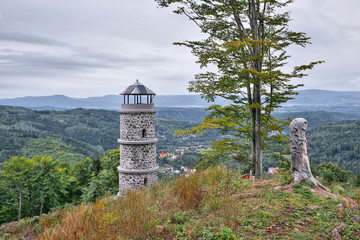 Big tree and stone lookout on top of Bucina hill with Ohre river valley and Ore mountains on background at beginning autumn czech