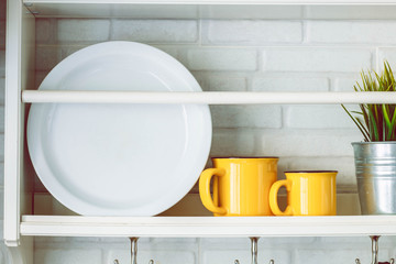 Yellow cups and white plates on the kitchen shelf white