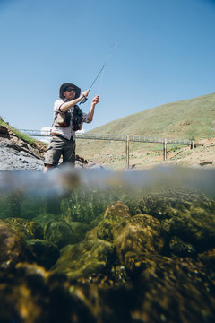 fly fisherman casting into a mountain river