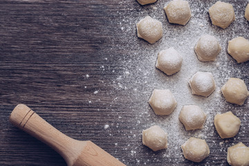 Fresh dumplings on a wooden surface with a wooden rolling pin. View from above