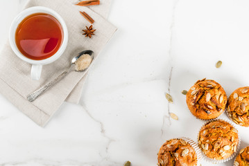 Autumn and winter baked pastries. Healthy pumpkin muffins with traditional fall spices, pumpkin seeds. With tea cup. White marble table, copy space top view