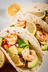Seafood. Mexican food. Tortilla tacos with traditional homemade salsa salad, parsley, fresh lemon, avocado and grilled shrimp pawns. On a white marble background.