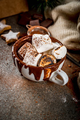 Fototapeta na wymiar New Year and Christmas treats. Traditional sweets. A cup of hot chocolate with marshmallow fried on fire, gingerbread stars, with sweater on black stone background, copy space