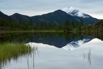 The reflection of snow-capped peaks in a mountain lake. Ridge Chersky, Yakutia, Russia.