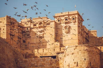 Foto op Plexiglas Vestingwerk Vogels die over de torens van historisch Jaisalmer-fort vliegen met monumentale steenmuren in oude stad van Rajasthan, India