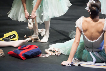 preparation, backstage, passion concept. on the stage of the theater female ballet dancers preparing to final rehearsal, wearing pointe shoes, putting ribbons and warming up