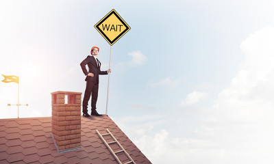 Young businessman on house brick roof holding yellow signboard. 