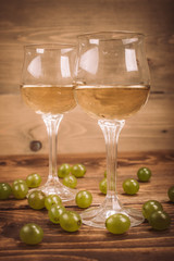 Two glasses of white wine and grapes on wooden table