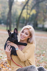 Beautiful and happy young blond woman enjoying in autumn park with her adorable French bulldog puppy. 