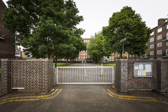 Horizontal picture from a residencial building with cloudy sky, with a gate in the front and a long passageway with trees located in London.