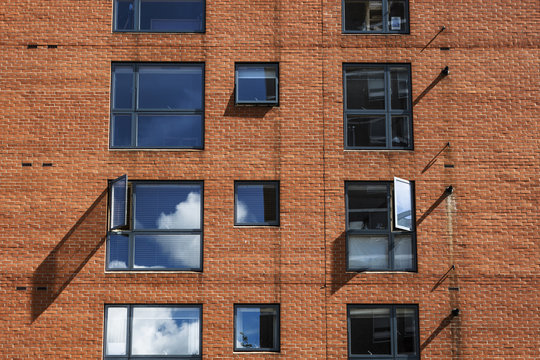 Horizontal picture of a building facade with orange bricks, windows with sky reflections in London.