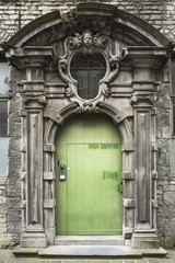A detail picture of a stained wooden green door with stone ornaments in Ghent, Belgium.