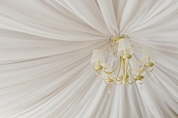 Classic chandelier hanging on ceiling made of white cloth. View from bottom.